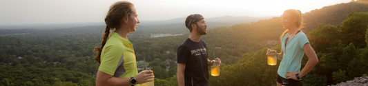 Runners on a mountain top drinking jars of Iced Piper and Leaf Golden Hour Tonic herbal blend