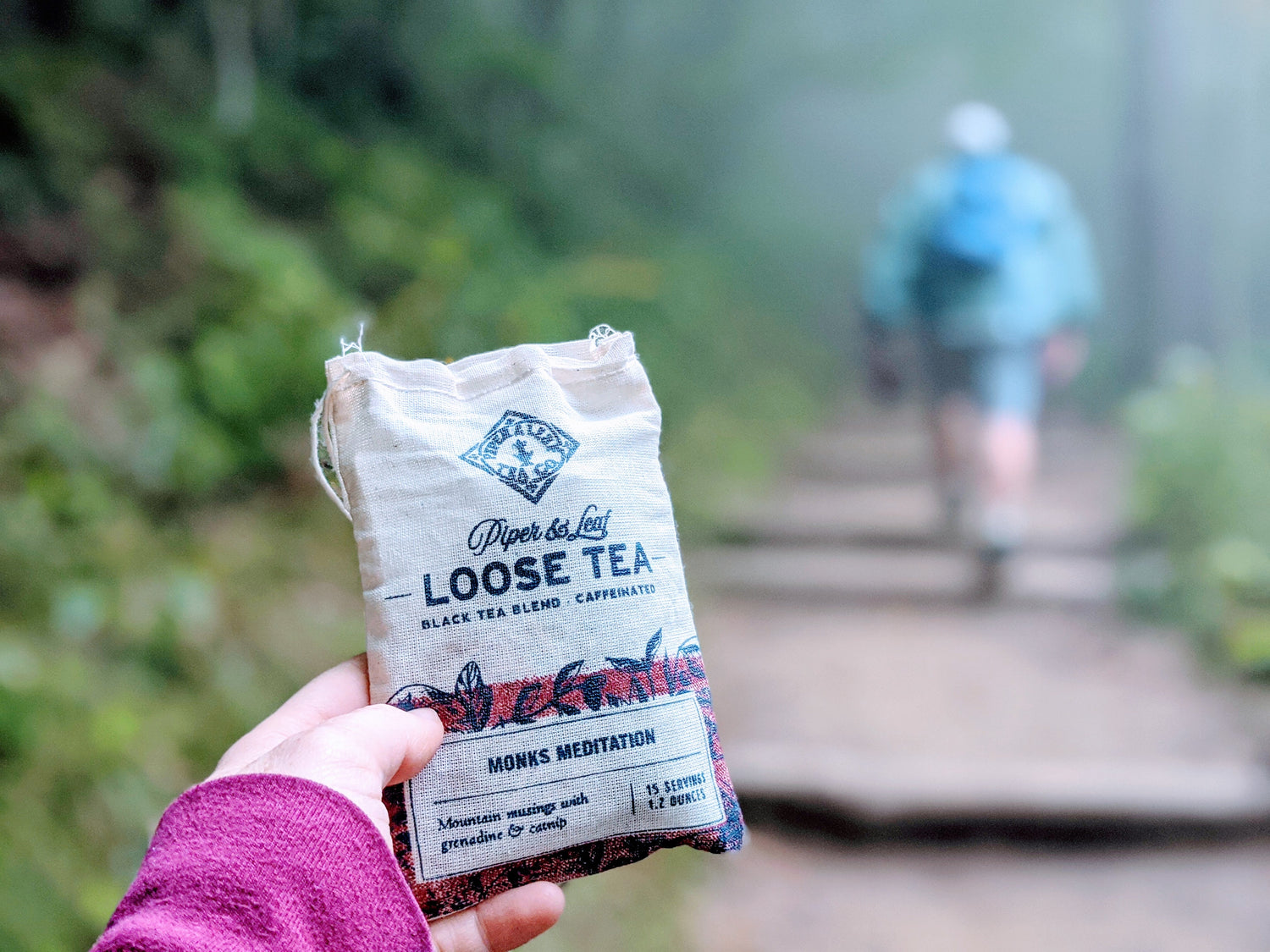 A person holding a bag of loose tea on a trail.