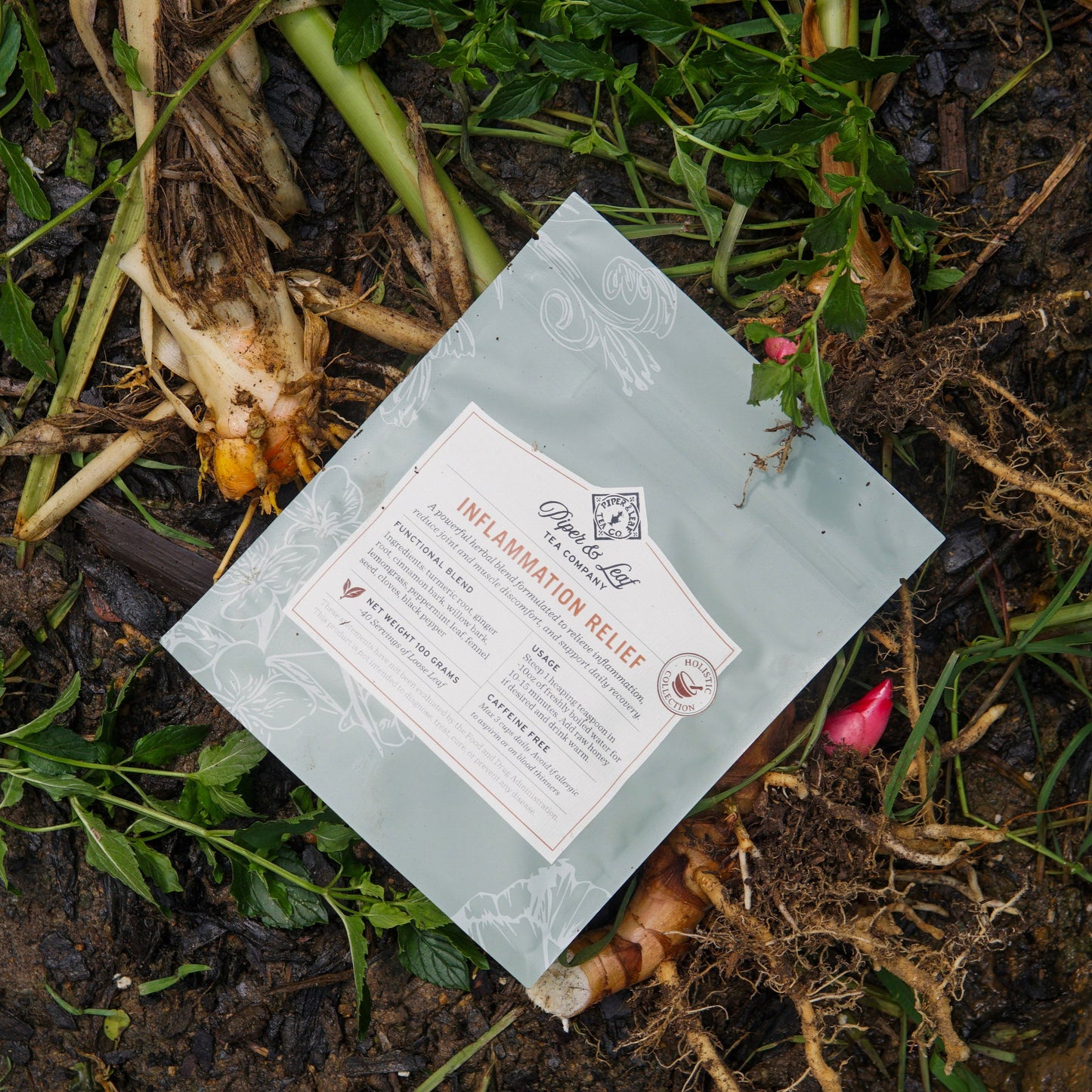 A packet of "Inflammation Relief" by Piper and Leaf Tea Co. rests among uprooted plant roots and green stems, suggesting a herbal blend crafted to help ease inflammation.
