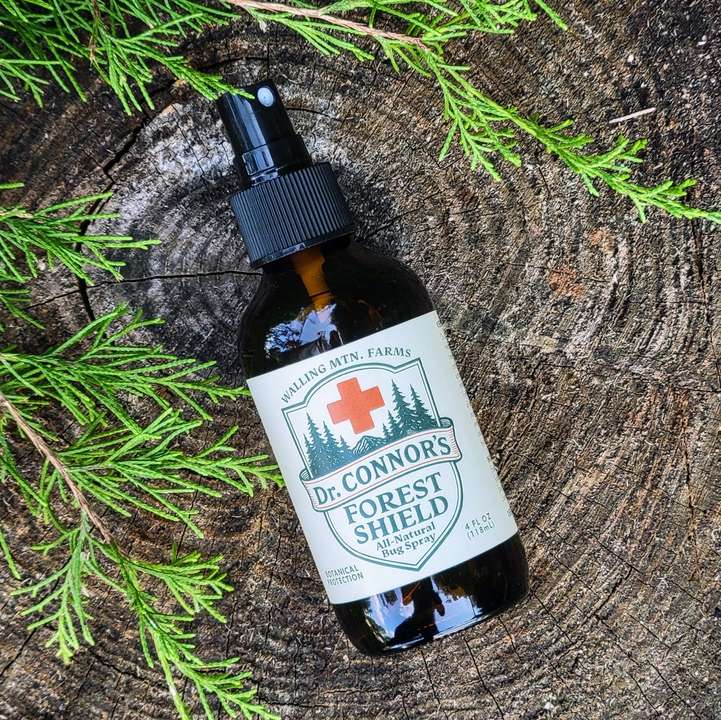 A brown bottle of Walling Mountain Farms’ Dr. Connor's Forest Shield All-Natural Bug Spray rests on a tree stump, surrounded by green foliage.