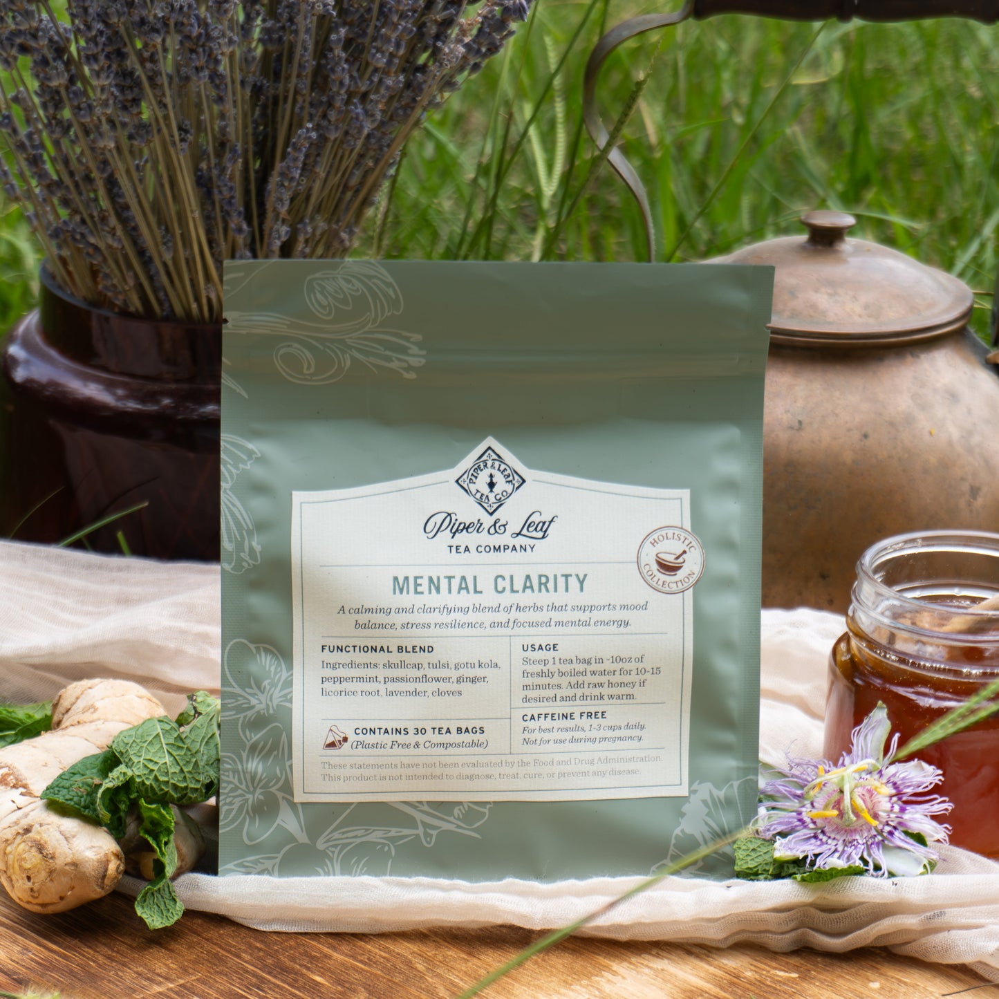 A bag of Piper & Leaf Tea Co. "Mental Clarity" tea rests outdoors with fresh herbs, ginger, honey, and a teapot—ideal for supporting mental energy and mood balance.