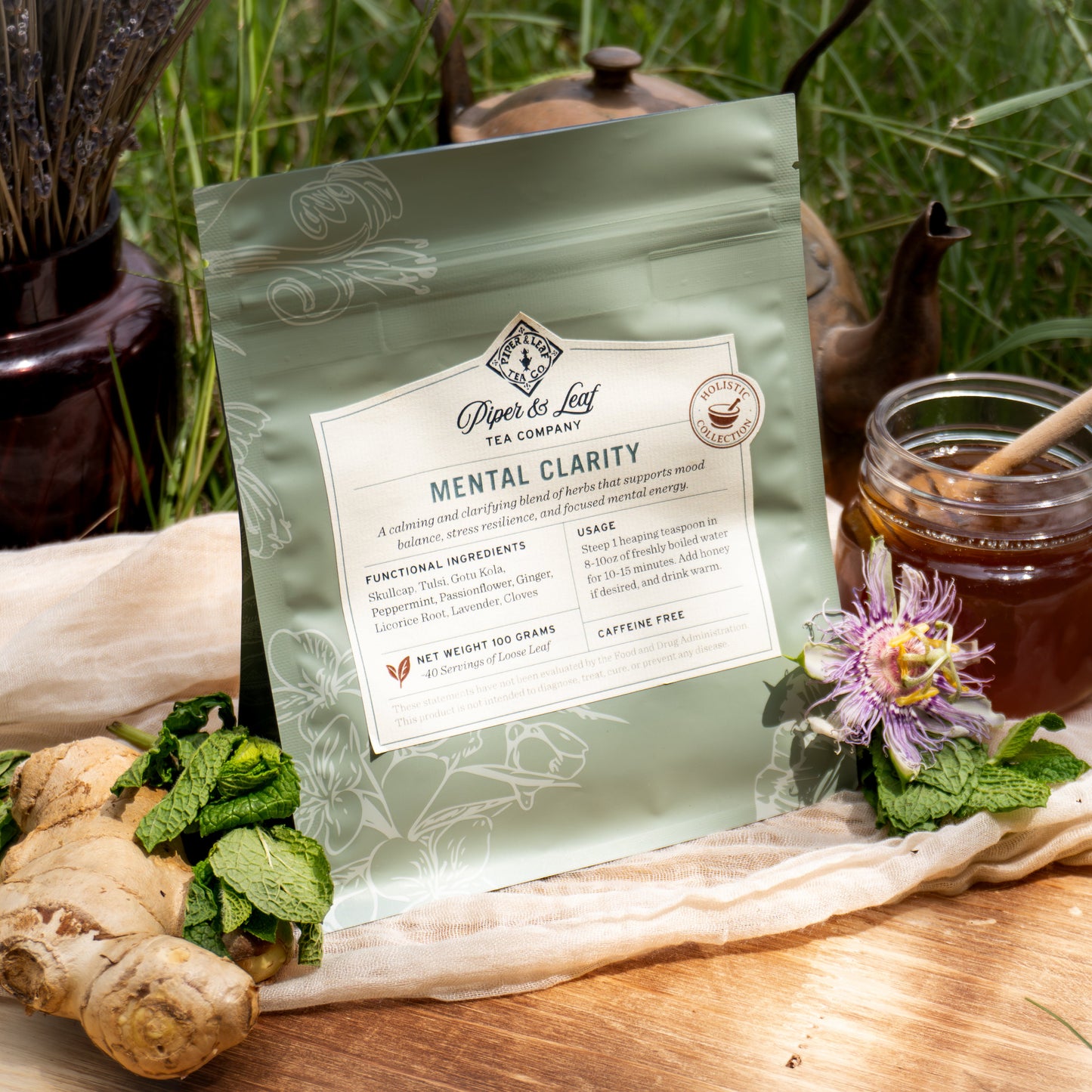 Piper & Leaf Tea Co.’s “Mental Clarity” tea is pictured outdoors with ginger, mint, a teapot, honey, and flowers, highlighting its support for stress resilience and mental energy in a peaceful setting.