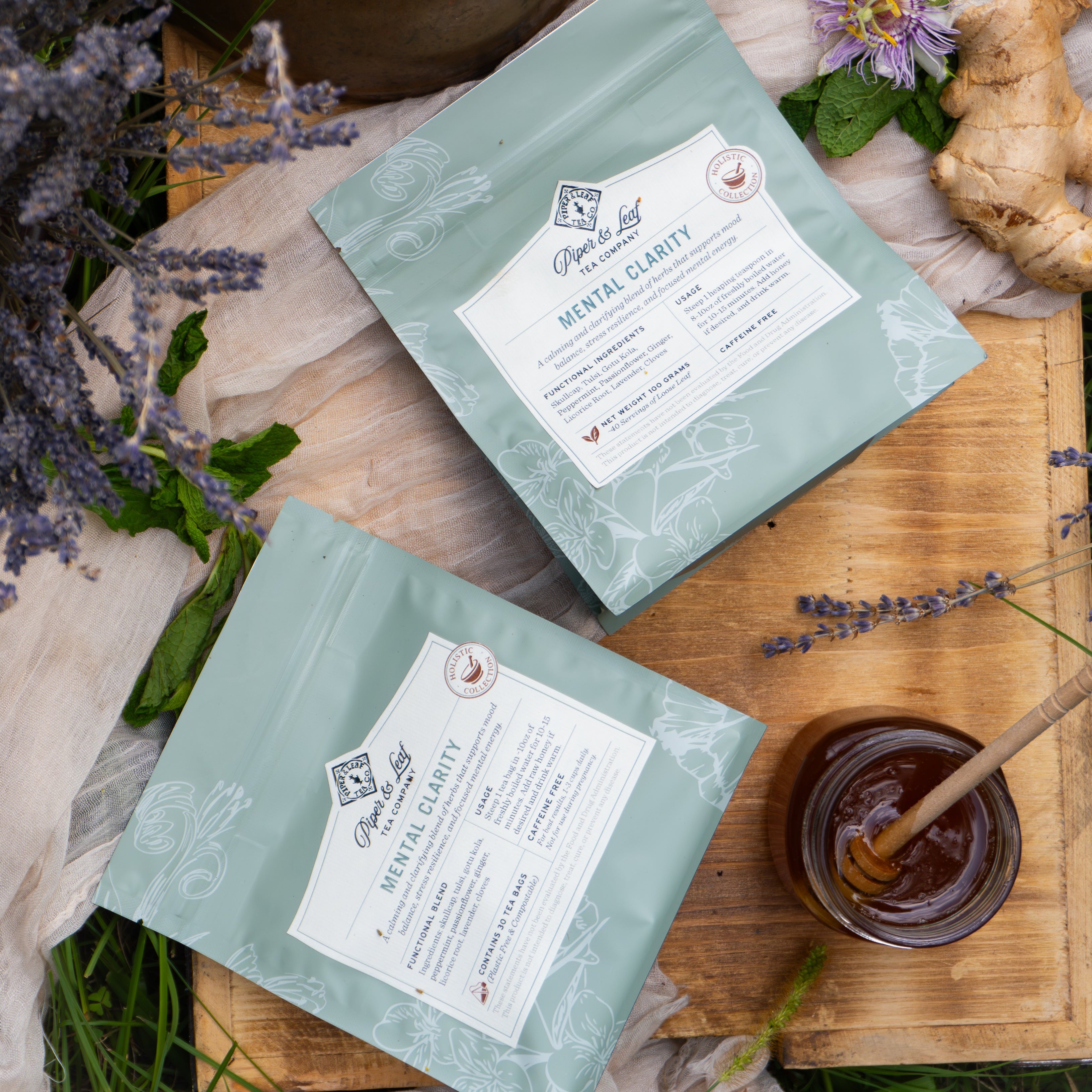 Two teal Piper & Leaf Tea Co. "Mental Clarity" herbal tea packages rest on wood amid lavender, ginger, greenery, and honey—blended to support mood balance and energize your day.
