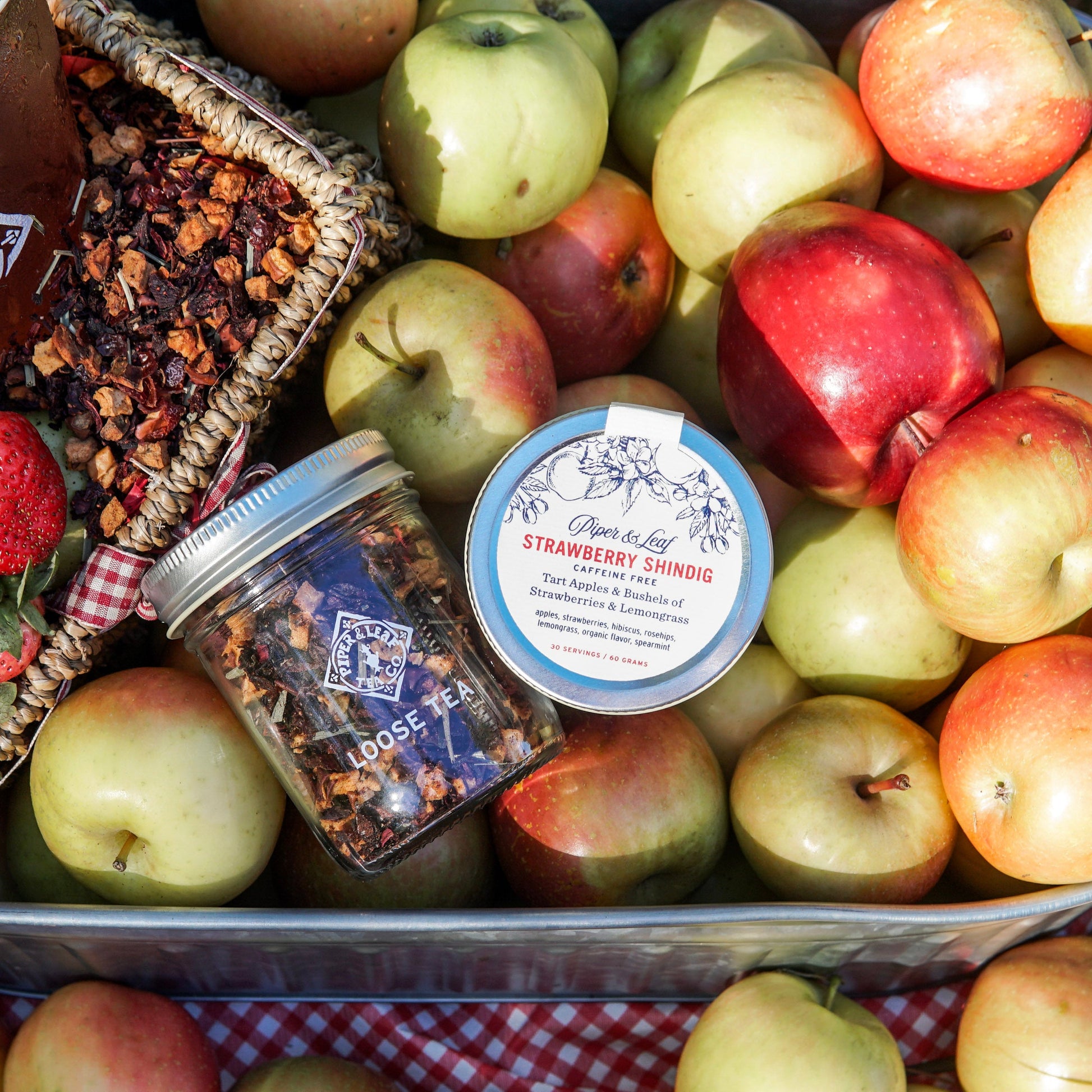 A Piper & Leaf Tea Co. "Strawberry Shindig" Glass Jar of Loose Leaf Tea (30 servings) sits among apples and dried fruit, promising a delightful, caffeine-free strawberry tea experience.