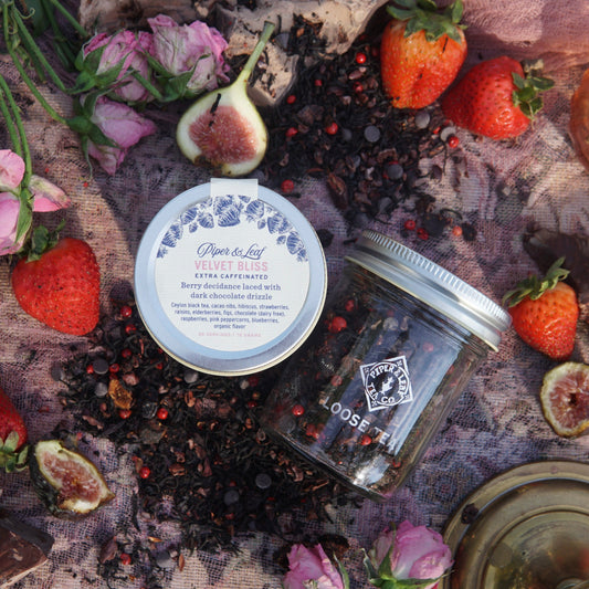 The Velvet Bliss Glass Jar of Loose Tea by Piper & Leaf Tea Co., displayed with dried tea ingredients, strawberries, and flowers, evokes the decadent aroma of chocolate-covered strawberry tea with rich creamy chocolate notes.