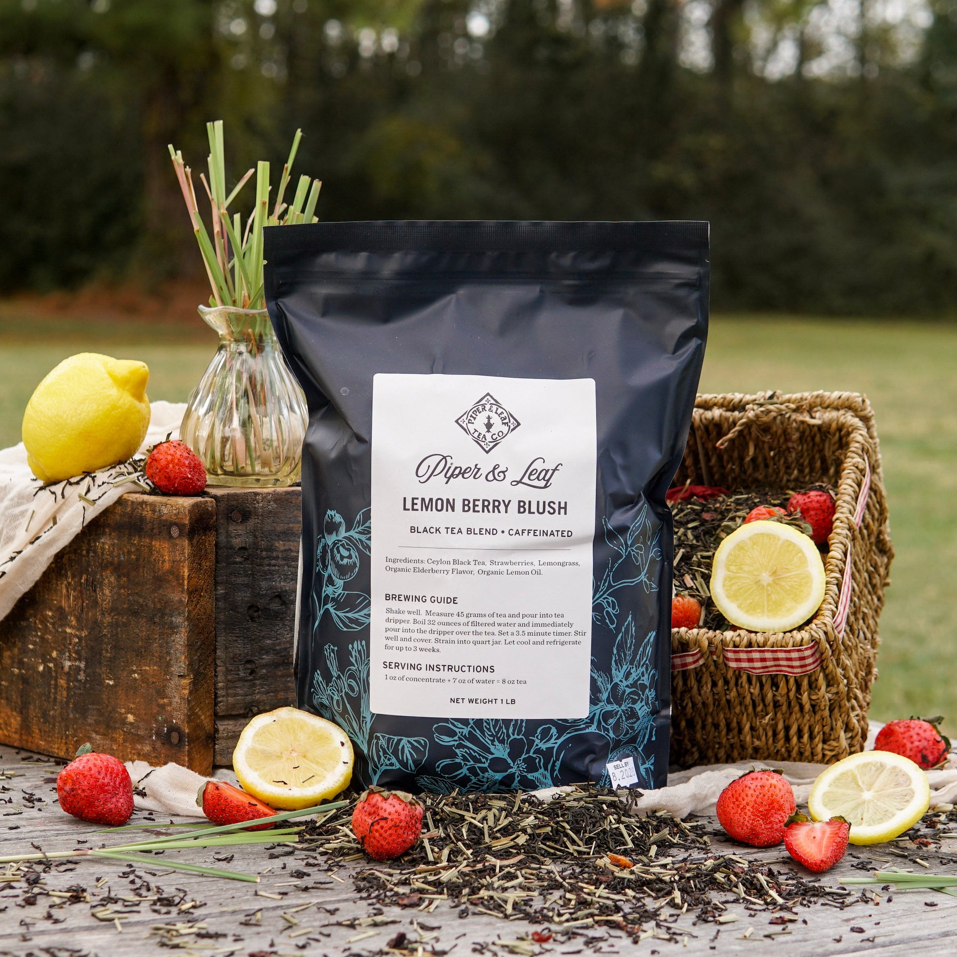 A Piper & Leaf Tea Co. Lemon Berry Blush Pound Bag (190 servings) is displayed outdoors on a table with fresh strawberries, lemons, loose leaf tea, and a basket.