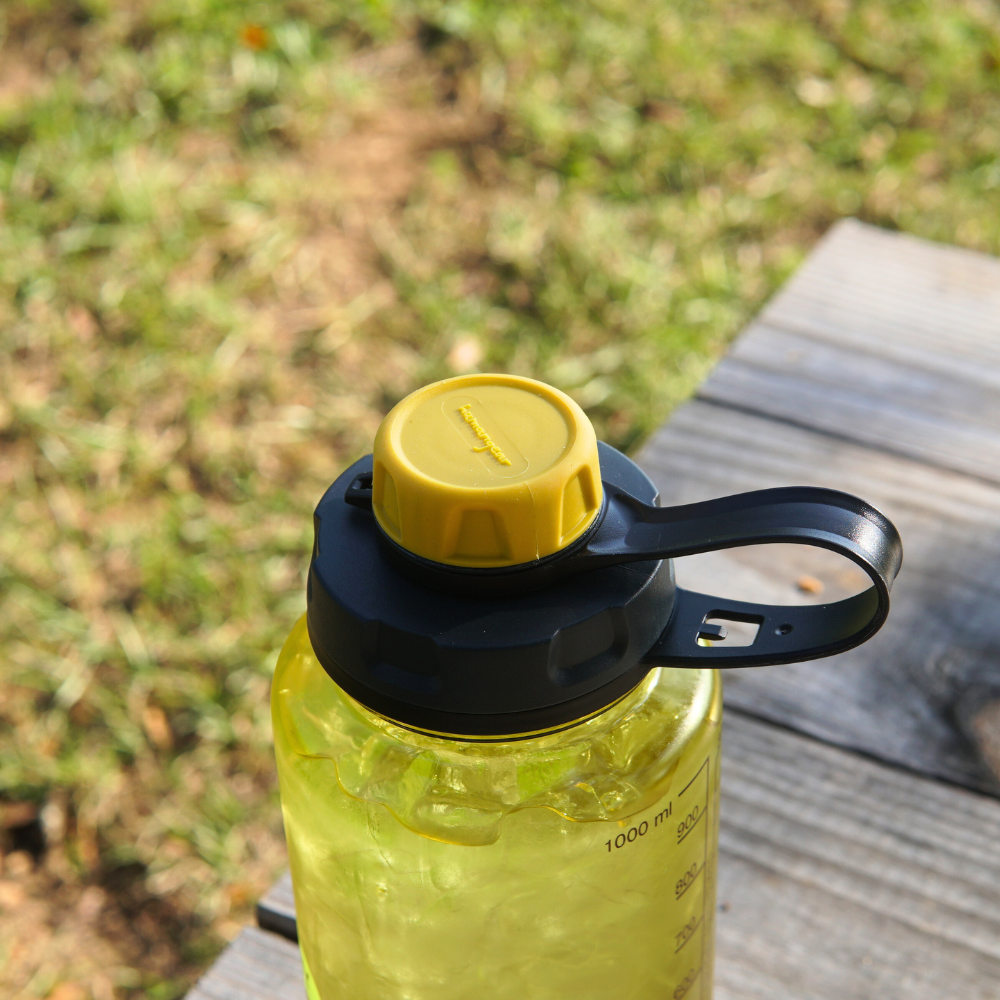A Nalgene capCap Lid from Piper & Leaf Tea Co., designed to be BPA-free, sits on a wooden surface with grass in the background, providing an ideal solution for splash-free sipping.