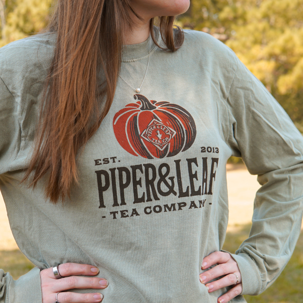 Person wearing a sage green Piper & Leaf Tea Co. Piper Pumpkin Comfort Colors Shirt outdoors—perfect for fall festivities.