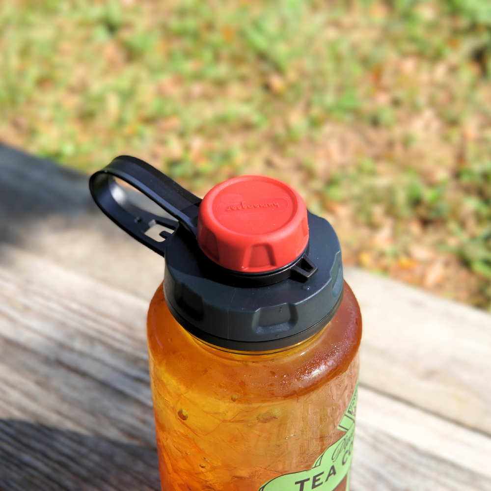 A BPA-free Piper & Leaf Tea Co. bottle with a Nalgene capCap Lid rests on a wooden surface, guaranteeing splash-free sipping for your daily adventures.