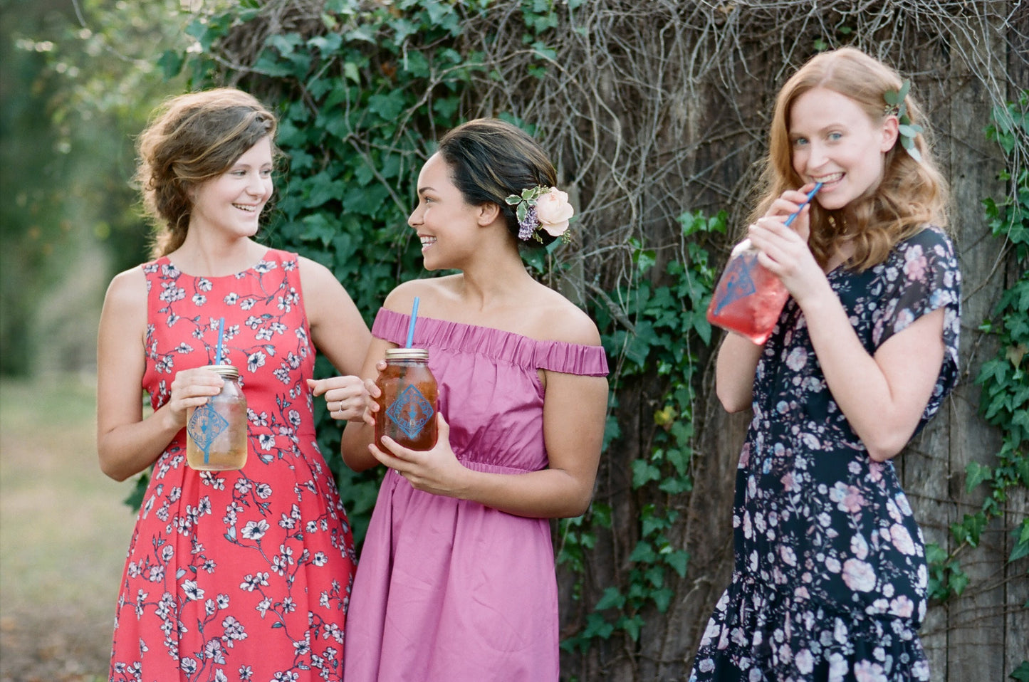 Three bridesmaids are standing next to each other, each holding a Signature Mason Drinking Jar - Quart Size filled with iced tea from Piper & Leaf Tea Co.