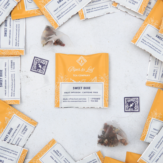 An individually wrapped tea bag surrounded by other wrapped tea bags of Piper and Leaf caffeine-free, Summer seasonal blend, Sweet Dixie. This blend has pineapple, coconut, and blueberries for a truly tropical blend reminiscent of a Piña Colada!