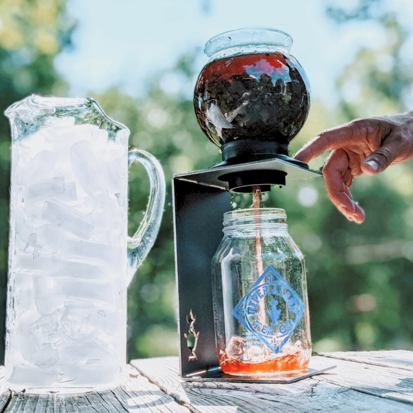 A person pouring ice into a JL Troupe Company Handmade Industrial Steel Dripper Stand.