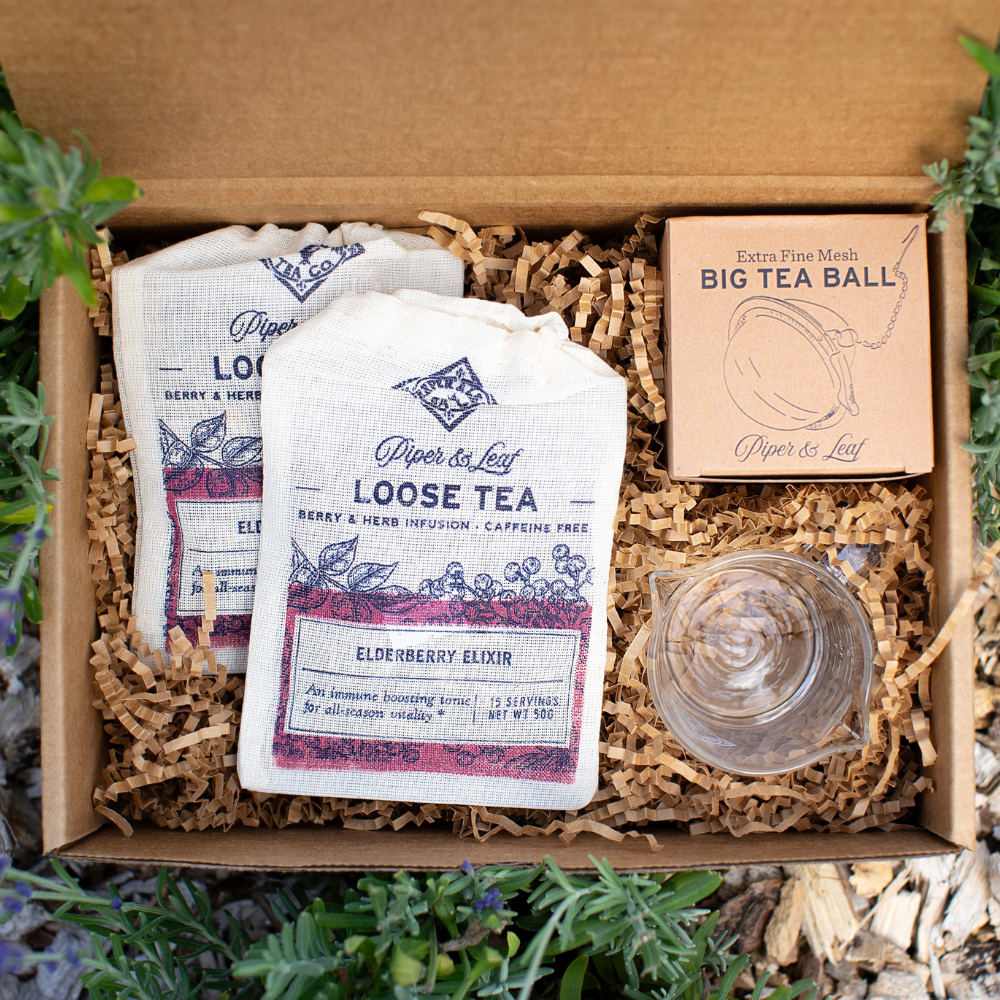 A Piper and Leaf Tea Co. Elderberry Syrup Starter Brewing Kit filled with tea bags and a glass of Elderberry Elixir Syrup tea.