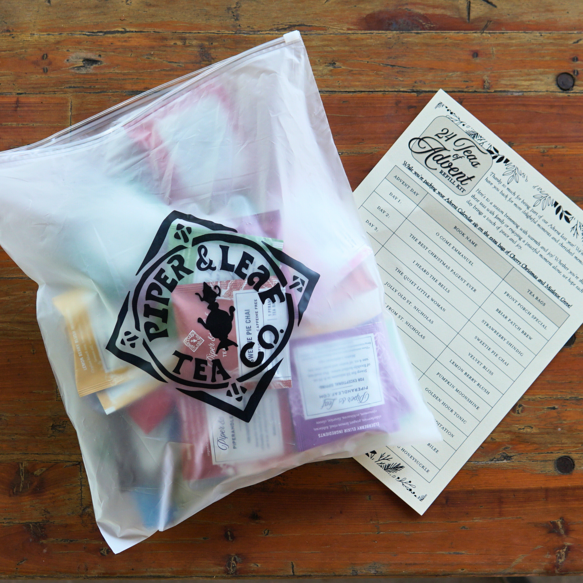 A clear Piper & Leaf Tea Co. bag labeled "Advent Calendar Refill Kit" contains artisan tea bags, placed beside a printed 24 Teas of Advent Calendar on a wooden surface.
