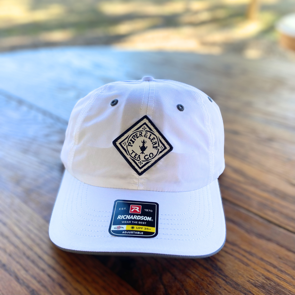 A white P&L Sport cap with a black logo on it from Piper & Leaf Tea Co.