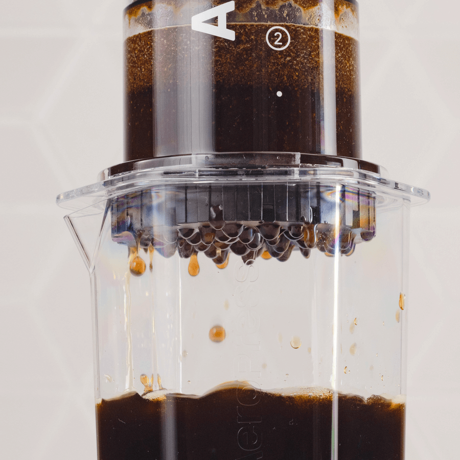 Close-up of coffee brewing in an AeroPress Clear XL Portable Coffee Press by AeroPress, showing rich coffee dripping from the filter into a clear container below.