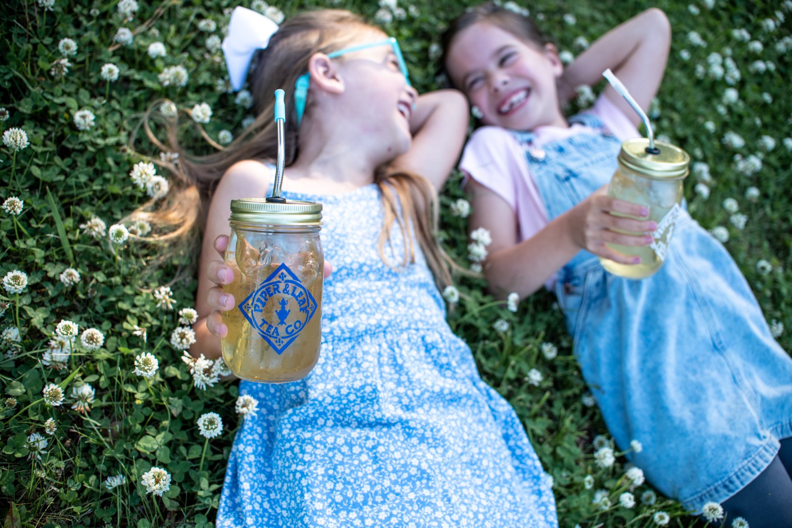 Two girls lounging in the grass with iced tea in Piper & Leaf Tea Co. Signature Mason Jars - Pint Size.