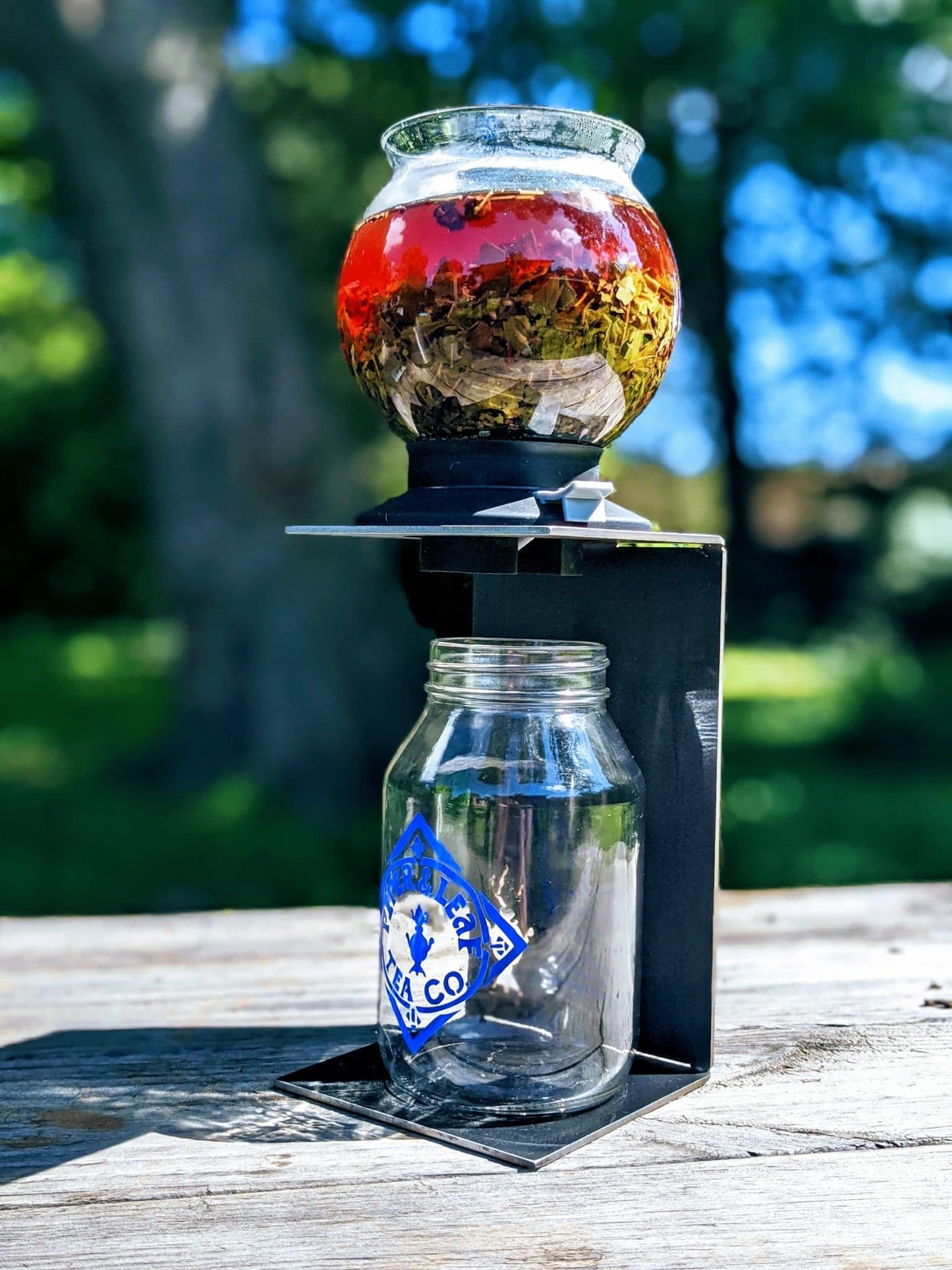 A tea dripper steeping concentrated tea on a steel drip stand over an empty quart jar