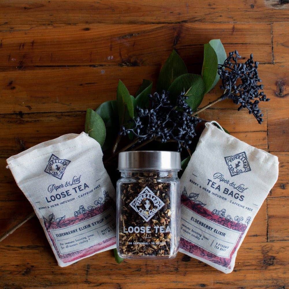 A Piper & Leaf Tea Co. Elderberry Elixir Glass Jar of Loose Leaf Tea- 30 Servings and a bag of tonic tea on a wooden table.