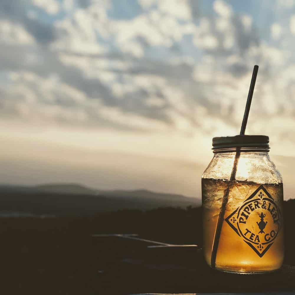 A Piper & Leaf quart jar of iced Golden Hour Tonic shines in the light of a sunrise over the mountains
