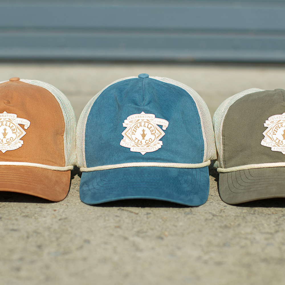 Three P&L Anniversary Soft Trucker Hats with embroidered logos on them, by Piper & Leaf Tea Co.