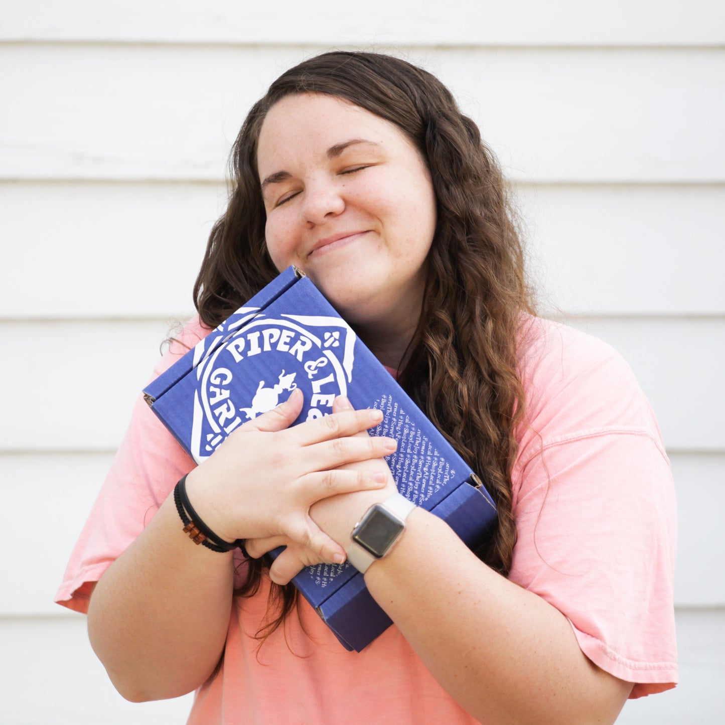 A woman holding a blue box with a smile on her face, containing Piper & Leaf Tea Co.'s Tea Subscription, an exquisite artisan tea.