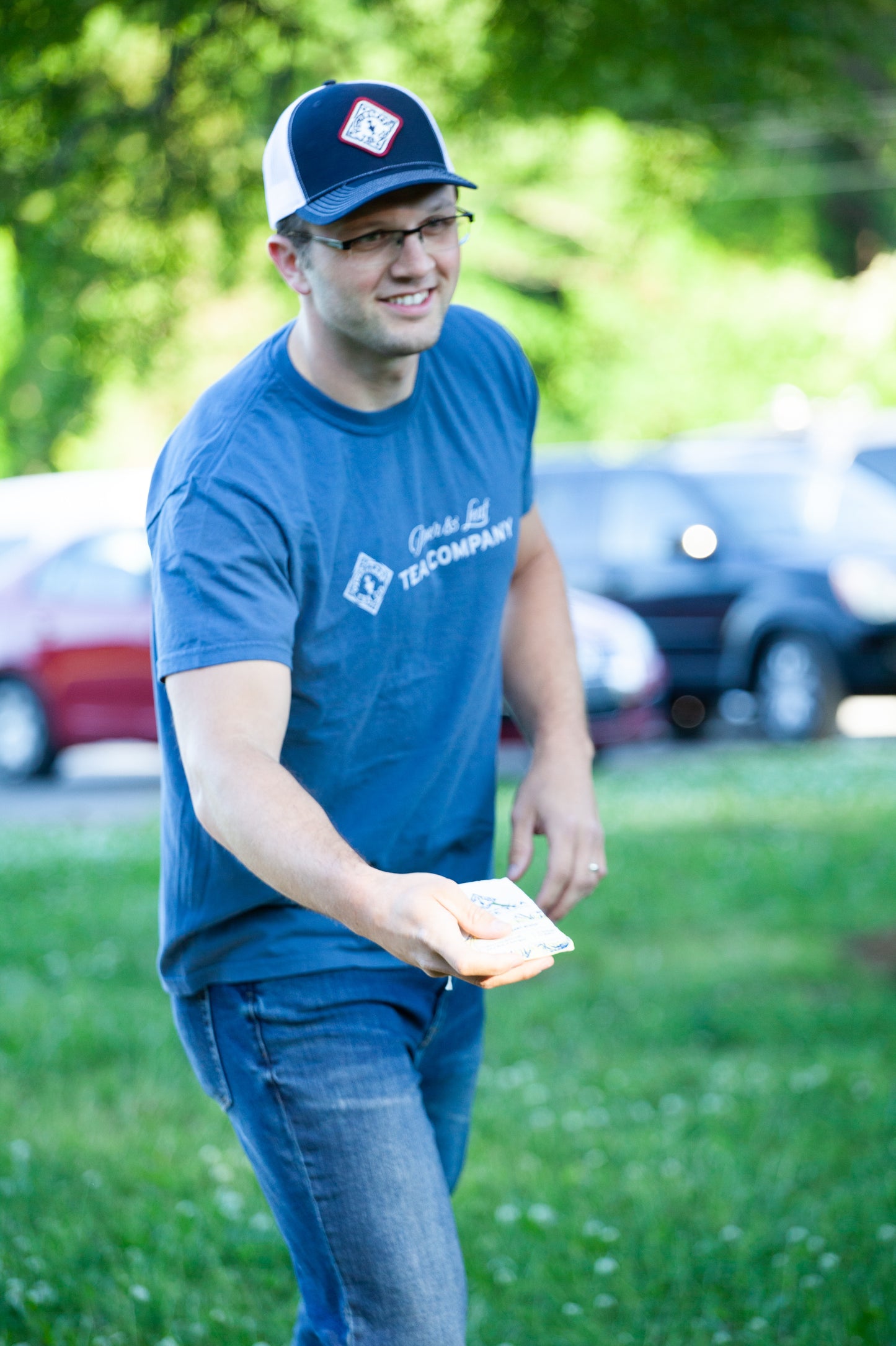 A man in a blue Piper & Leaf tee-shirt and a blue ballcap throws a beanbag