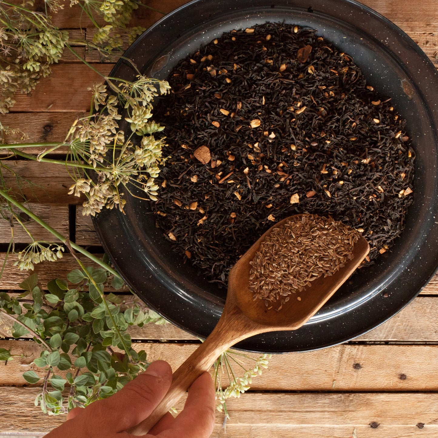 A wooden spoon scoops more spices into a bowl of blended tea and spices