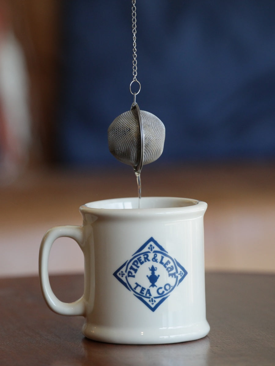A tea ball strainer, full of loose leaf, being pulled out of a Piper & Leaf mug