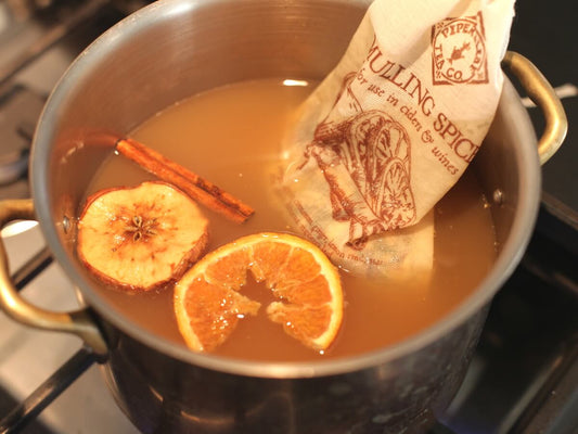 Mulling spices steeping in a pot of apple cider with cinnamon stick, apple slice, and orange slice as garnishes