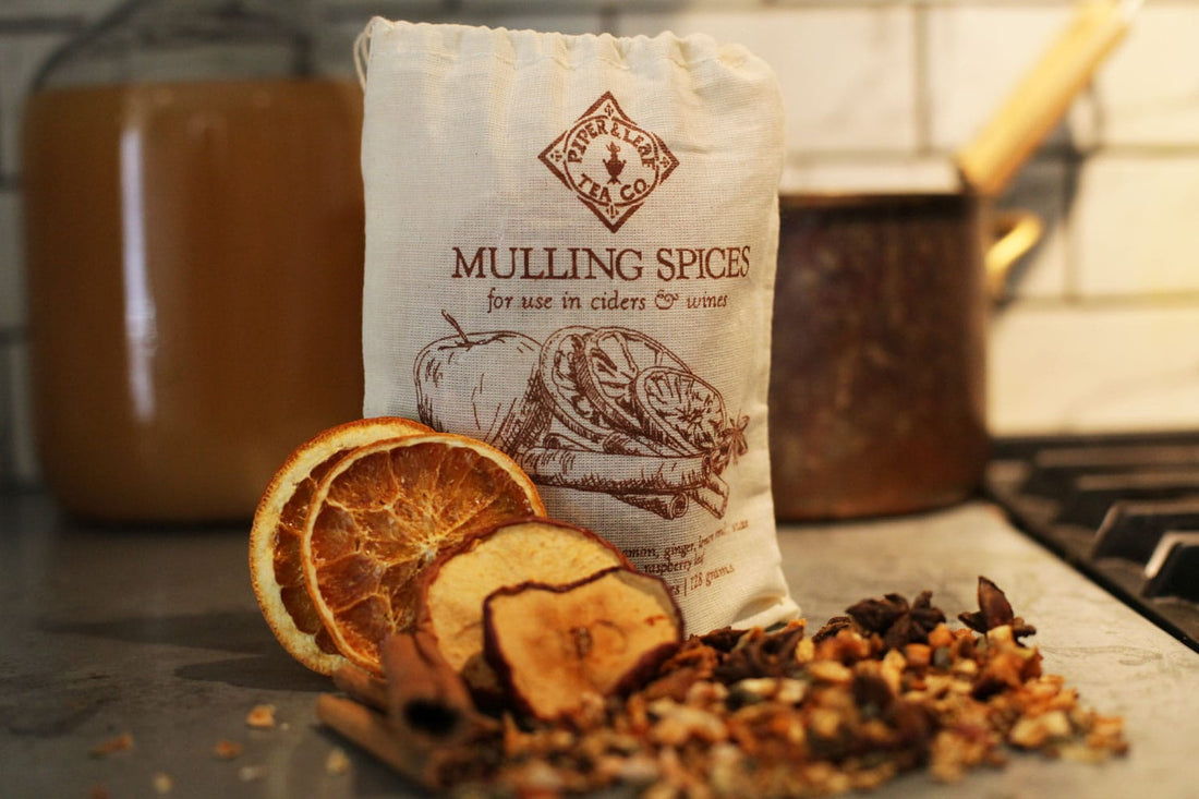 A bag of Piper & Leaf mulling spices sits behind a pile of dried orange slices, dehydrated apples, cinnamon sticks, and various chai spices