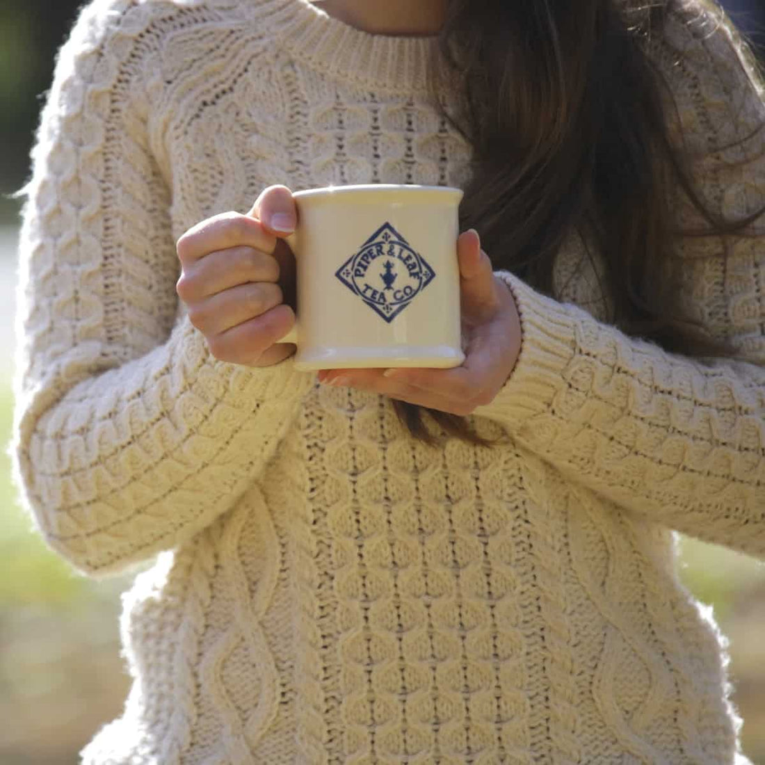 A girl in a thick sweater holds a mug of Piper & Leaf tea for warmth