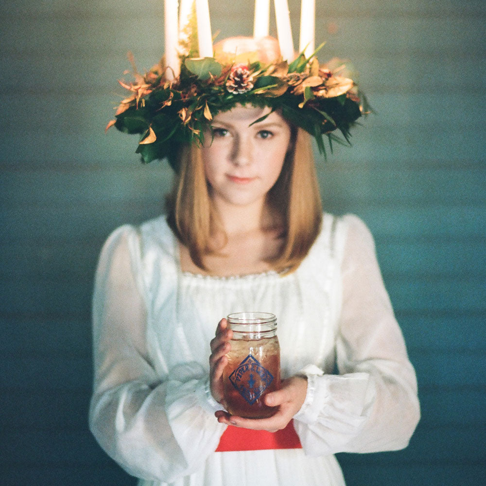 A woman wearing a wreath and holding a jar of candles.