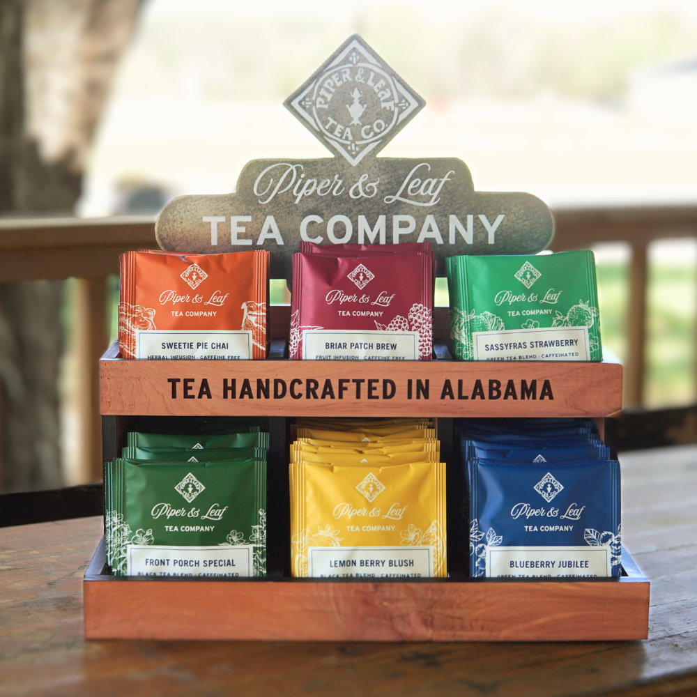 Display of Piper & Leaf Tea Company handcrafted tea pouches in Alabama. Six flavors are showcased in an organized wooden stand.