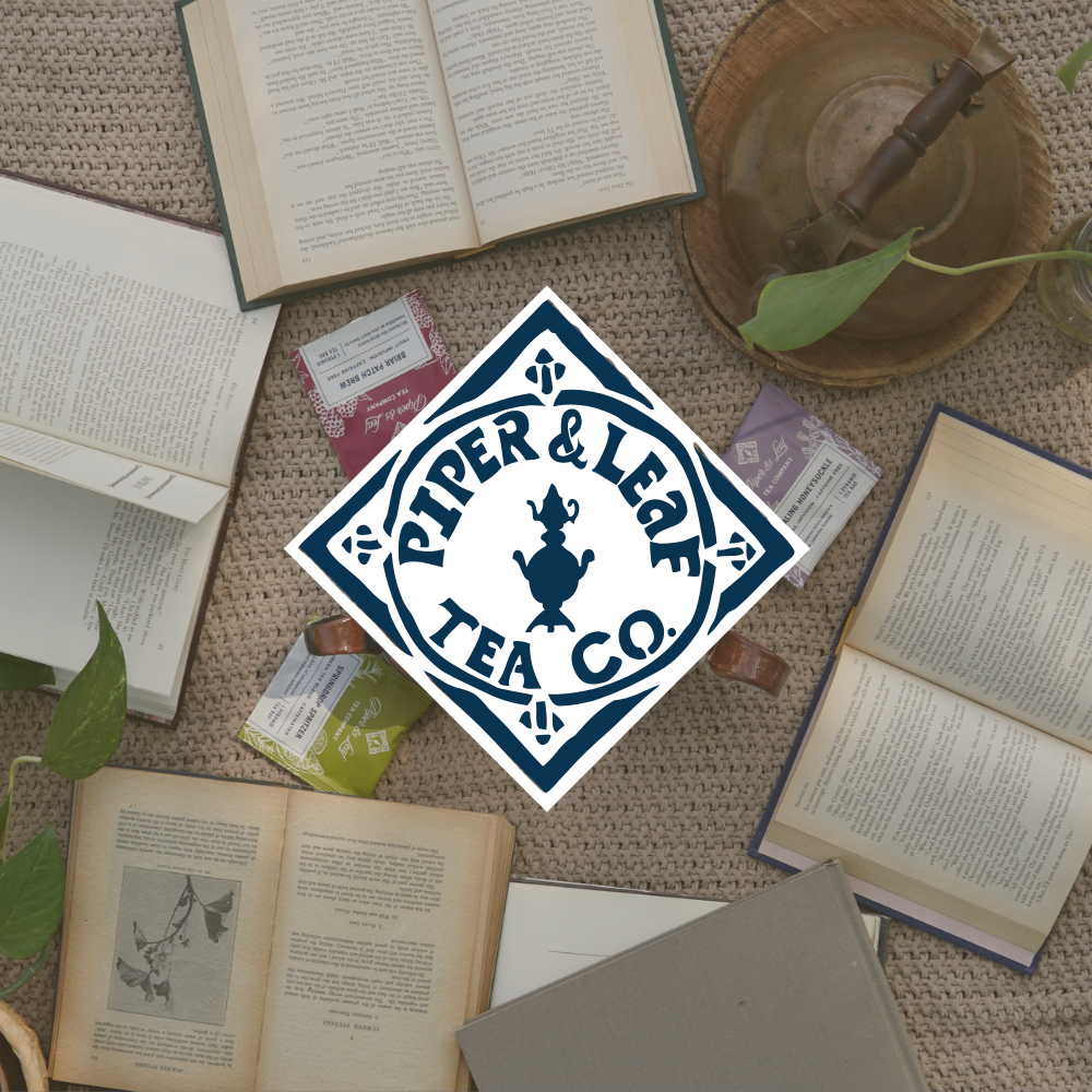 Open books and tea packets arranged on a textured surface with scattered green leaves, overlaid by the Piper & Leaf Tea Co. logo in the center.