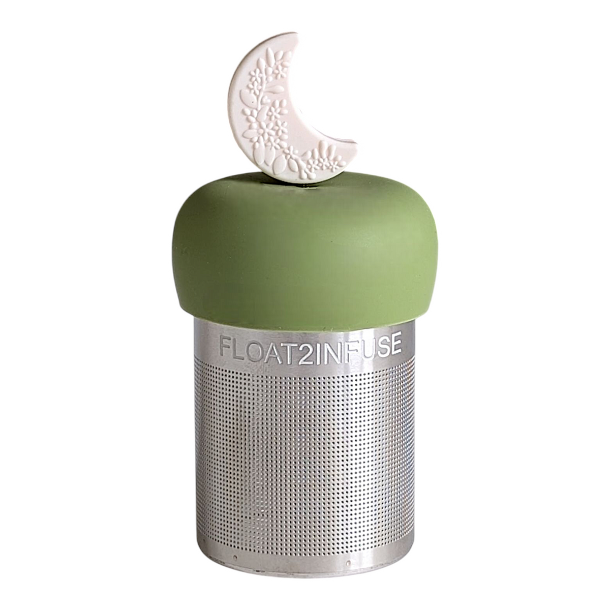 The Float2infuse Tea Infuser Ivory Floral Crescent Moon - Floating Tea Infuser features a metal design with a green silicone top, adorned with a white crescent moon embossed with floral details, making it the ideal loose-leaf tea accessory for your daily brew.