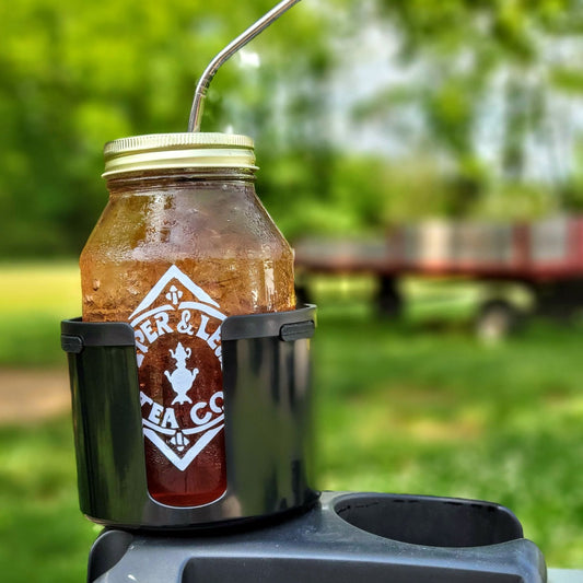 A Piper and Leaf Tea Co. Mason Jar Cup Holder Adapter - Keep Your Jar in the Car with a straw sitting on top of it.