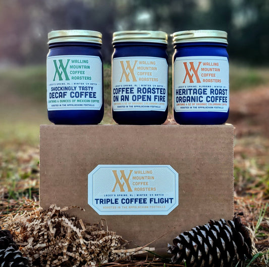 Three jars of Walling Mtn. Coffee, showcasing a diverse roast selection, sit atop a box labeled "Triple Coffee Flight by Walling Mtn. Roasters," with pine cones in the foreground.