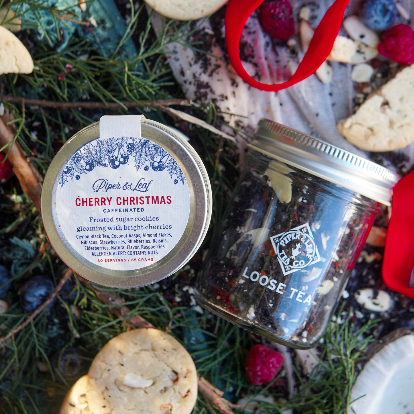 A Piper & Leaf Tea Co. Cherry Christmas Glass Jar of Loose Leaf Tea (30 servings) sits among pine branches, berries, cookies, and a red ribbon.