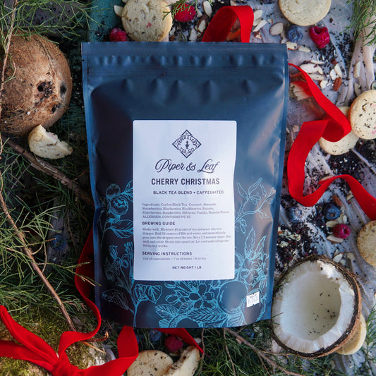 A Cherry Christmas Pound Bag—190 servings of loose leaf tea by Piper & Leaf Tea Co.—rests on a natural surface with cookies, coconut shells, red ribbon, and greenery.