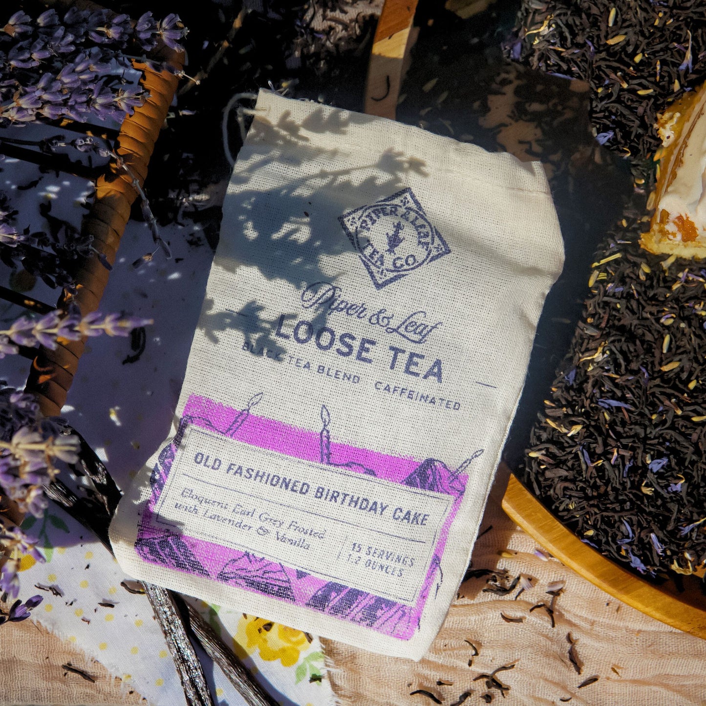 A Piper & Leaf Tea Co. "Old Fashioned Birthday Cake" Muslin Bag of Loose Leaf Tea (15 servings) sits on a table with loose leaf tea and sprigs of lavender.