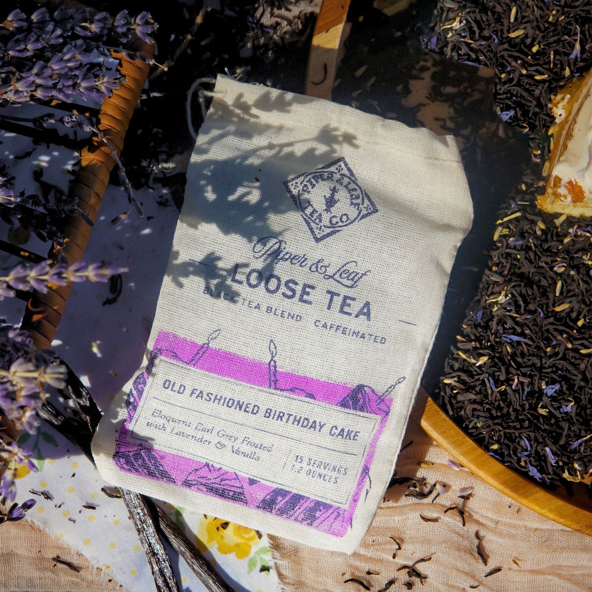 A Piper & Leaf Tea Co. "Old Fashioned Birthday Cake" Muslin Bag of Loose Leaf Tea (15 servings) sits on a table with loose leaf tea and sprigs of lavender.