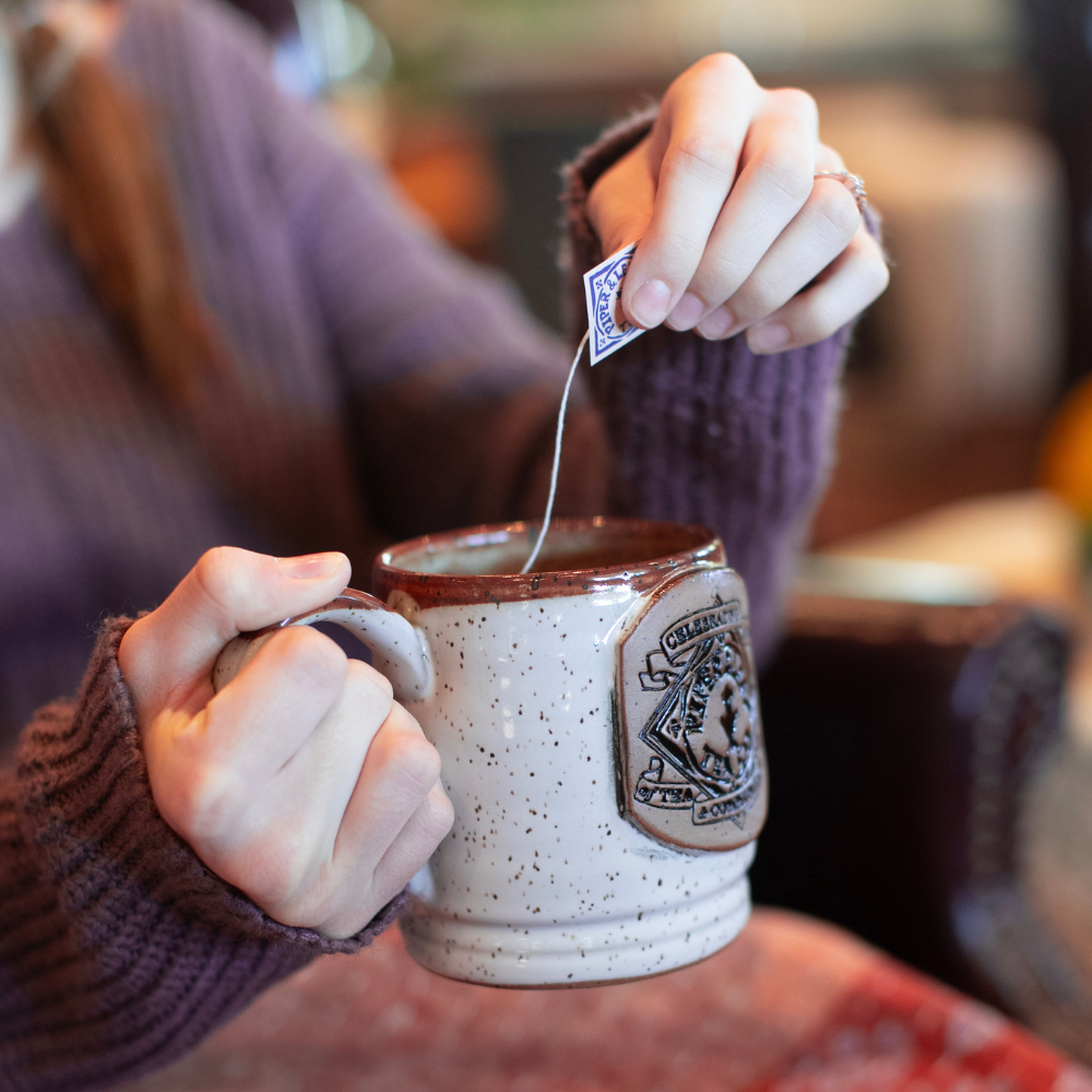 A woman is holding a Piper & Leaf Tea Co. Handmade 10th Anniversary Pottery Mug.