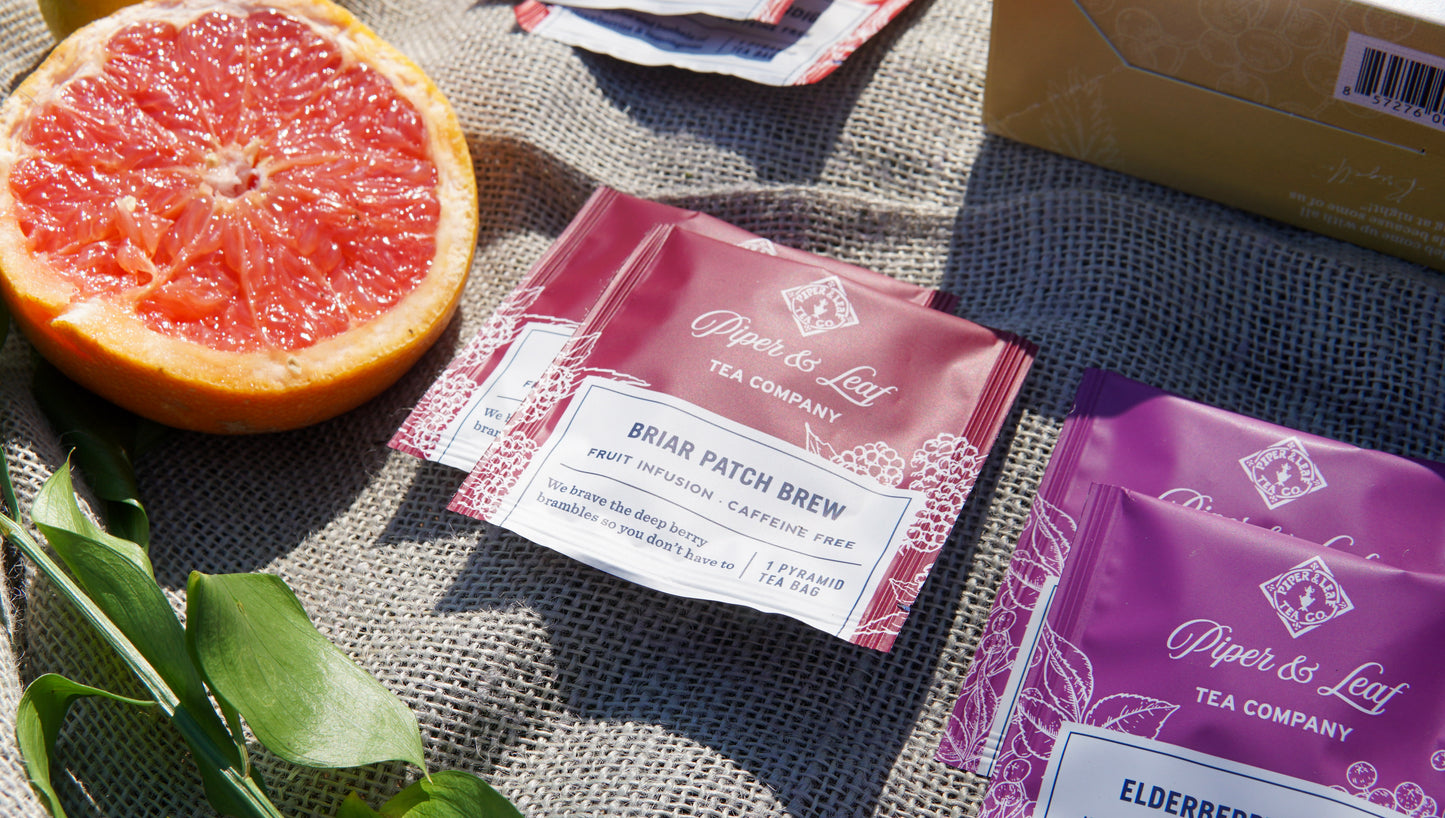 Piper & Leaf Tea Co.'s Caffeine Free Sampler—Box of 16 Tea Bags—is displayed on burlap with a halved grapefruit and green leaves.