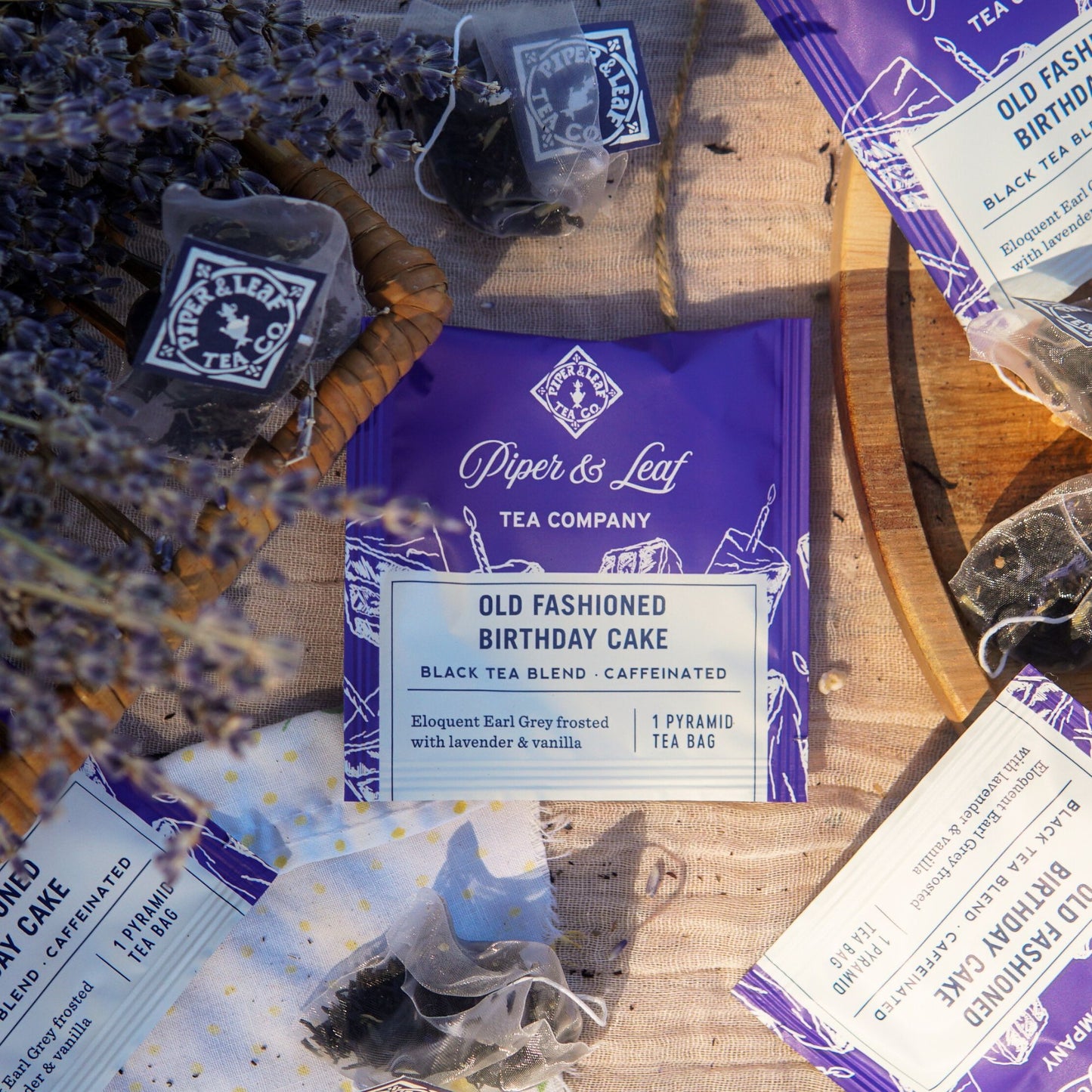 A flat lay of Piper & Leaf Tea Co. "Old Fashioned Birthday Cake" Case of Individually Wrapped Tea Bags (50ct) on a wooden surface with dried lavender.