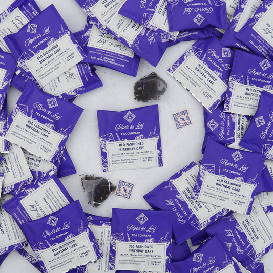 A pile of purple and white Piper & Leaf Tea Co. Old Fashioned Birthday Cake Case of Individually Wrapped Tea Bags- 50ct sachets.