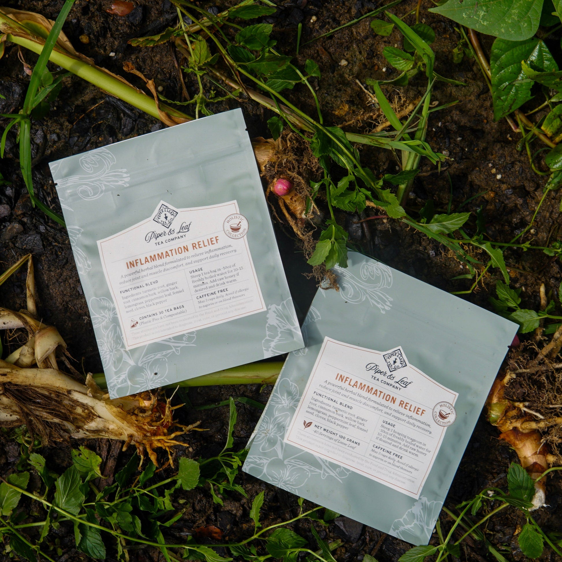 Two packets of "Inflammation Relief" herbal tea by Piper and Leaf Tea Co. lay on soil amid green plants and exposed roots, highlighting the soothing blend’s natural setting.