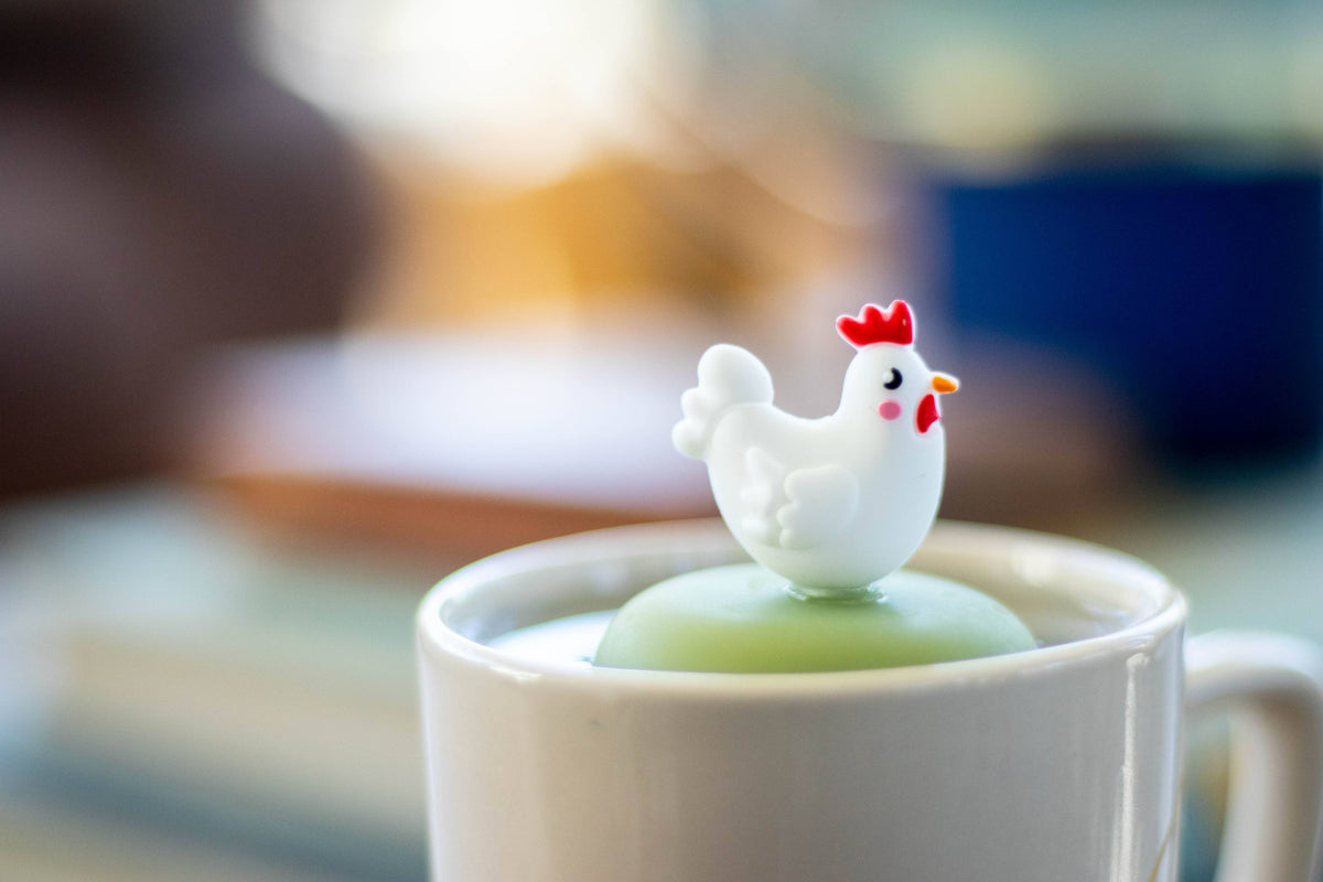 Enjoy a whimsical teatime with the Float2infuse Tea Infuser’s Chicken - Floating Tea Infuser. This charming white mug comes with a green lid and is topped with an adorable plastic chicken figurine—white with a red comb and yellow beak—designed to steep your favorite loose-leaf tea in style. Elevate your tea routine with this delightful and playful accessory.
