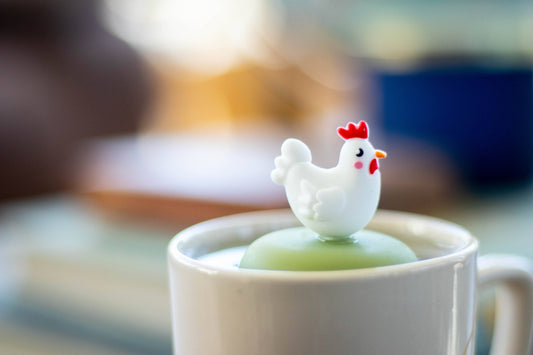 Enjoy a whimsical teatime with the Float2infuse Tea Infuser’s Chicken - Floating Tea Infuser. This charming white mug comes with a green lid and is topped with an adorable plastic chicken figurine—white with a red comb and yellow beak—designed to steep your favorite loose-leaf tea in style. Elevate your tea routine with this delightful and playful accessory.