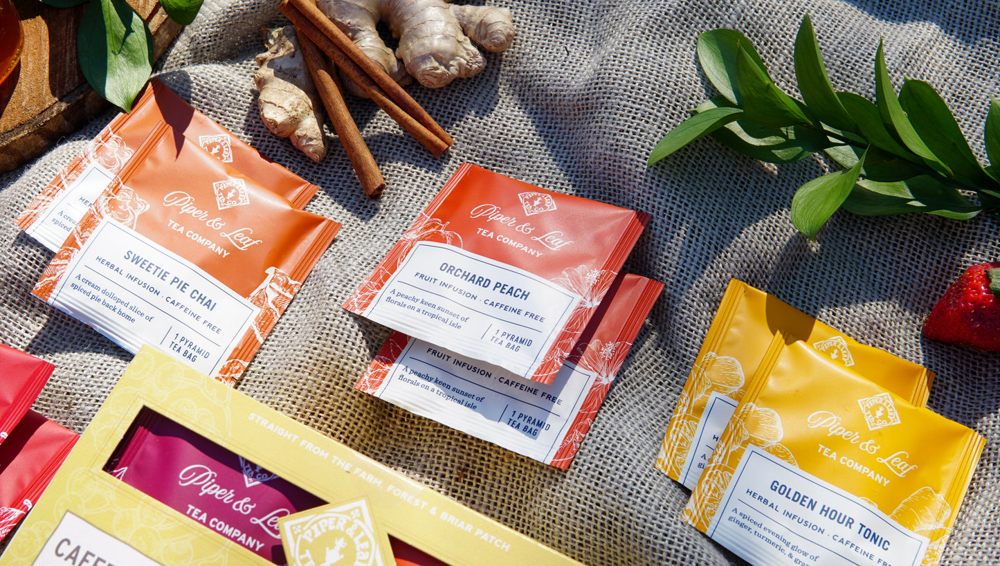 The Piper & Leaf Tea Co. Caffeine Free Sampler (box of 16 tea bags) features vibrant herbal blends, displayed with ginger, cinnamon sticks, and green leaves for a unique tea tasting experience.